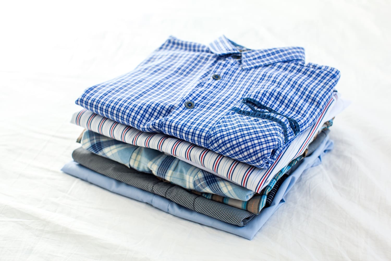 A neatly folded stack of collared shirts in various patterns and colors on a white surface.