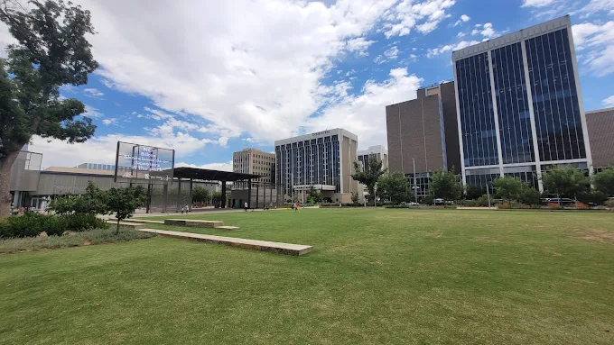 A green lawn with benches in front of modern office buildings under a partly cloudy sky.