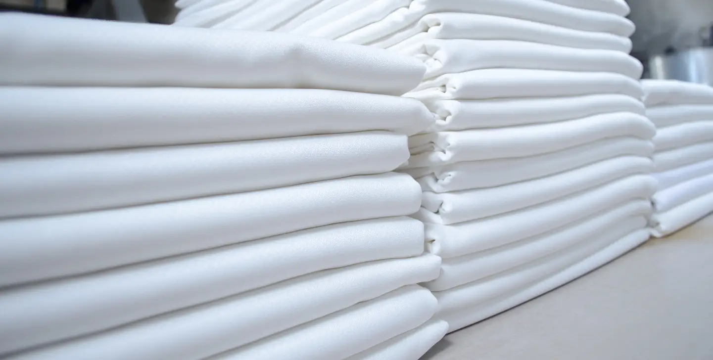Neatly stacked white towels arranged in two rows on a flat surface, showing the clean and orderly folds of each towel.